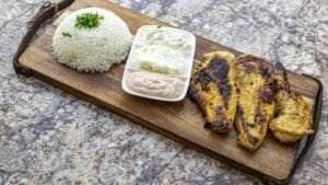 Healthy grilled chicken with rice and flavorful sauce on a wooden board.