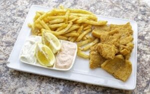 Mediterranean fish and chips on a white plate with lemon wedges.