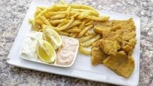 Seafood dish of fish and chips served on a white plate with lemon wedges.