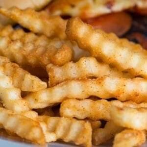 Close-up macro shot of crinkle-cut French fries stacked on a plate, showcasing their lightly seasoned, crispy texture.