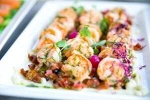Closeup of delicious shrimps with vegetables and microgreens on white plate on catering table