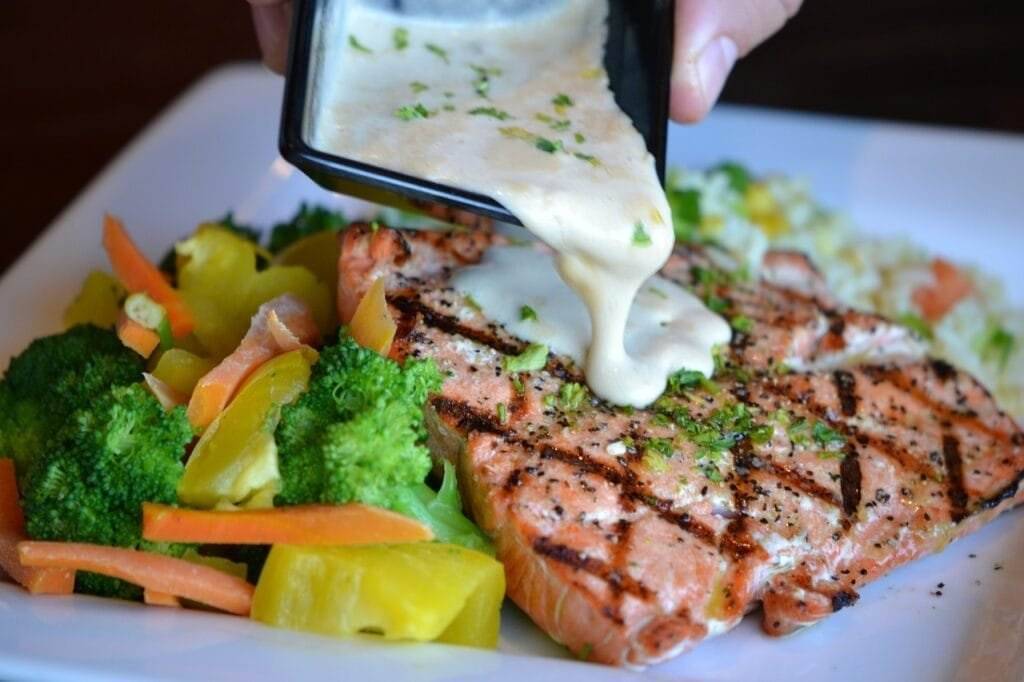 A person is drizzling a sauce on a plate of food. salmon, food, healthy-1312372.jpg