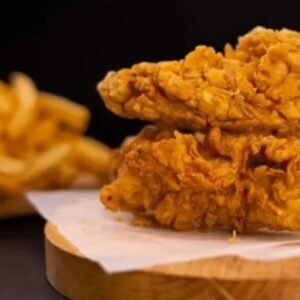 Two crispy Chicken Tenders with Fries rest on a wooden board, served alongside golden French fries on parchment paper.