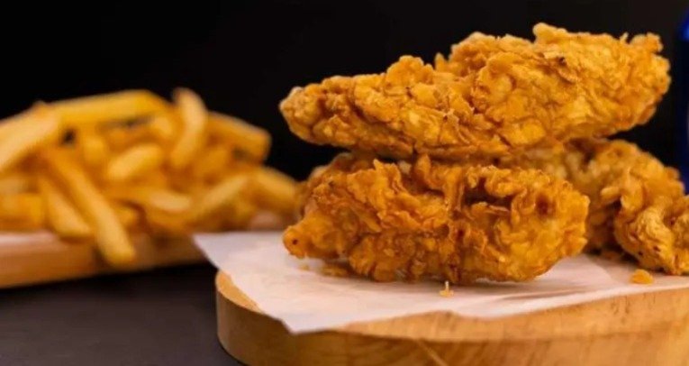 Two crispy Chicken Tenders with Fries rest on a wooden board, served alongside golden French fries on parchment paper.